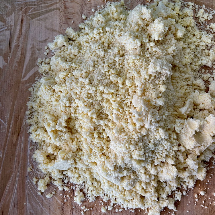 Image of To form the dough lay a big square of plastic wrap down onto your work surface and deposit the crumbly mixture into the center. 